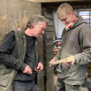 Master wheelwright Nick Gill and newly-qualified wheelwright Ted Shepherd look at a spoke before sanding.